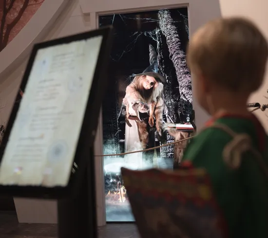 Kind betrachtet Hexenausstellung mit Zauberbuch im fantasievollen Museum